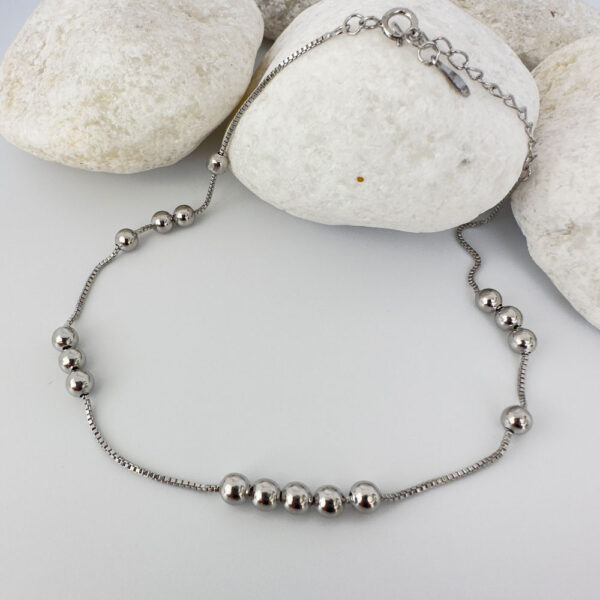 Silver anklet with identical balls floating around the chain, on white rocks.