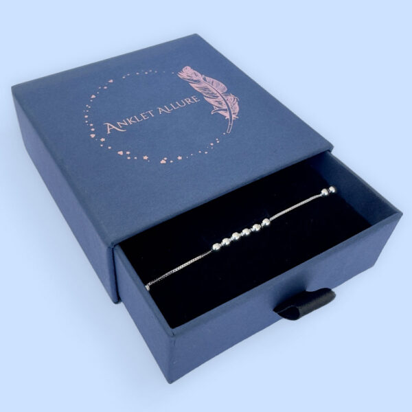 Silver anklet with identical balls floating around the chain, in a blue Anklet Allure jewellery box.
