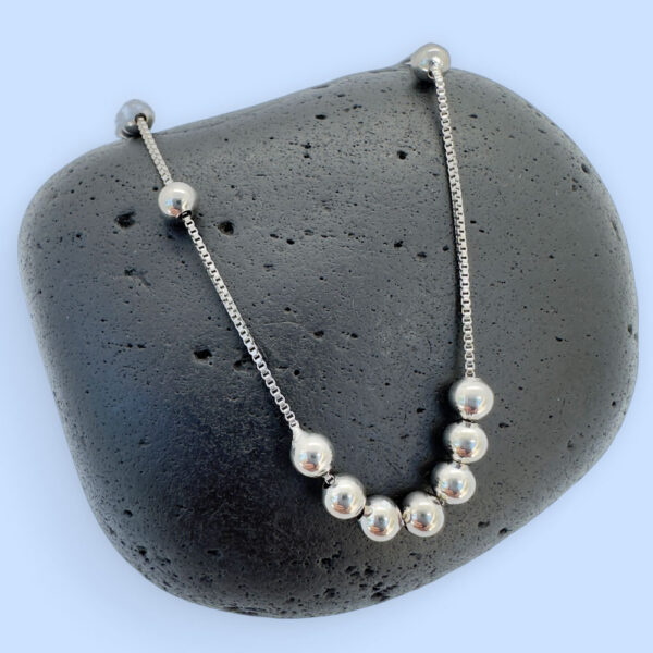 Silver anklet with identical balls floating around the chain, on a black rock.