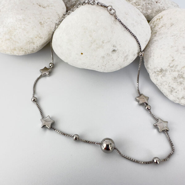 Silver anklet with solid star and ball charms on white rocks.
