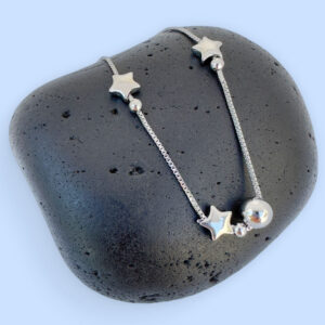 Silver anklet with solid star and ball charms on a black rock.