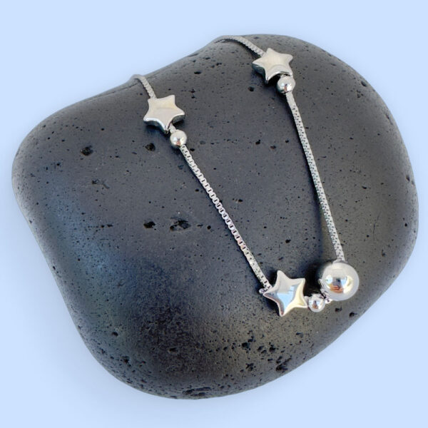 Silver anklet with solid star and ball charms on a black rock.