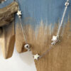 Silver chain with solid silver stars and two silver balls on a beachy wooden background.
