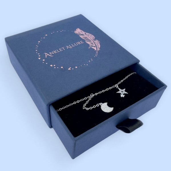 Ankle bracelet with a five pointed star and a crescent moon, both diamond encrusted, presented in a blue box.