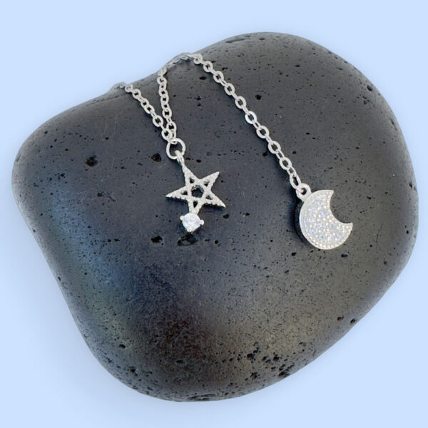 Ankle bracelet with a five pointed star and a crescent moon, both diamond encrusted, displayed on a black rock.