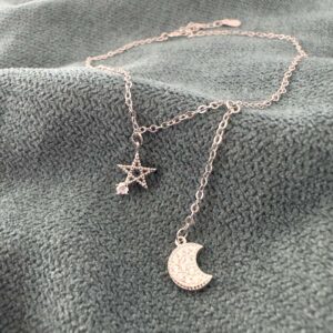 A simple silver chain with a five pointed star pendant with a cubic zirconia gemstone attached to one of the points and a cubic zirconia encrusted moon hanging down lower off the ankle chain.