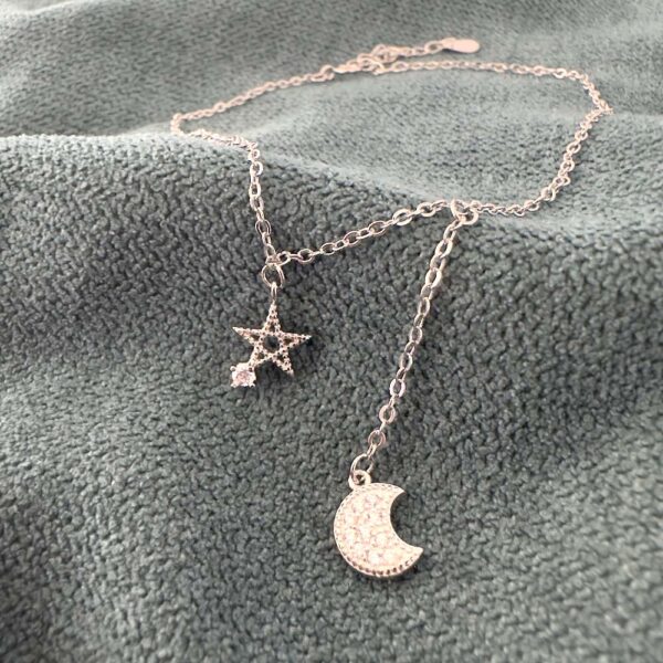 A simple silver chain with a five pointed star pendant with a cubic zirconia gemstone attached to one of the points and a cubic zirconia encrusted moon hanging down lower off the ankle chain.