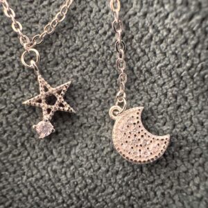 Close up of a five pointed star pendant with a cubic zirconia gemstone attached to one of the points and a cubic zirconia encrusted moon on an ankle bracelet.