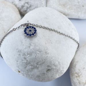 Ankle bracelet in silver with a round charm with blue and white gemstones and three round balls either side on white rocks.