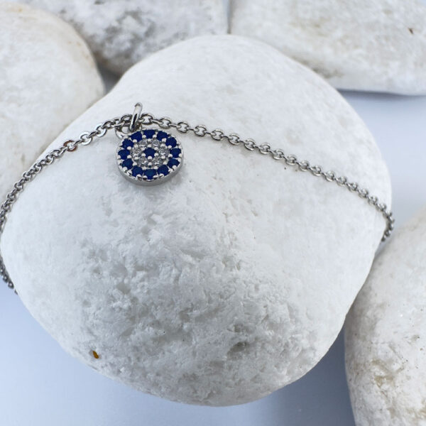 Ankle bracelet in silver with a round charm with blue and white gemstones and three round balls either side on white rocks.