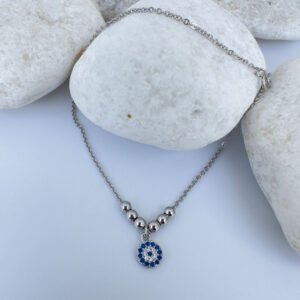 Anklet in silver with a round charm with blue and white gemstones and three round balls either side on a white rock.