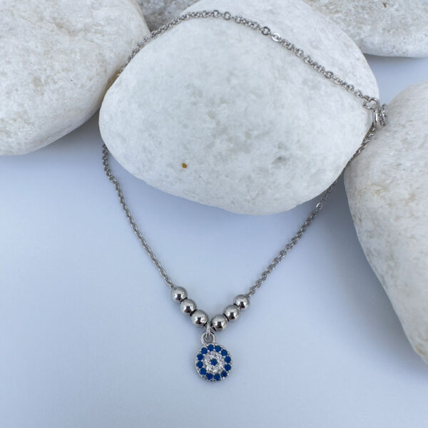 Anklet in silver with a round charm with blue and white gemstones and three round balls either side on a white rock.