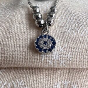 Close up of silver anklet with three silver balls either side of a round pendant which has a circle of blue gems around a circle of white gems and a blue single stone in the centre.