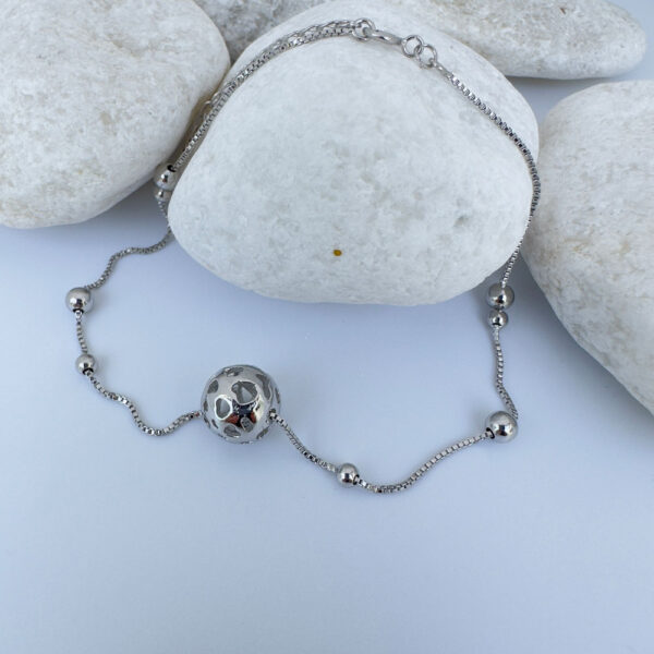 Silver anklet with a silver sphere and four silver balls on white rocks.