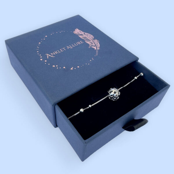 Silver anklet with a silver sphere and four silver balls presented in a dark blue Anklet Allure gift box.