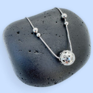 Silver anklet with a silver sphere and four silver balls on a black rock.