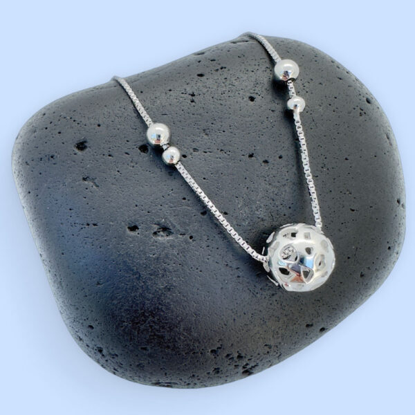 Silver anklet with a silver sphere and four silver balls on a black rock.