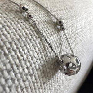 Silver anklet with a globe like ball as the main feature and two pairs of smaller balls one bigger than the other on a grey background.