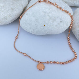 Rose gold anklet with a round pendant on a white rock.