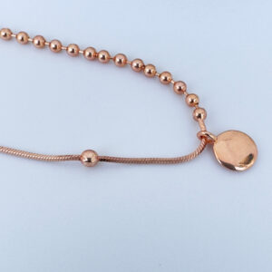 Close up of a rose gold anklet with a round charm and lots of small balls.