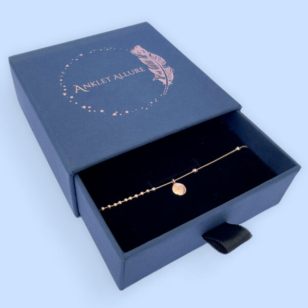 Rose gold anklet with a round pendant presented in a dark blue Anklet Allure gift box.