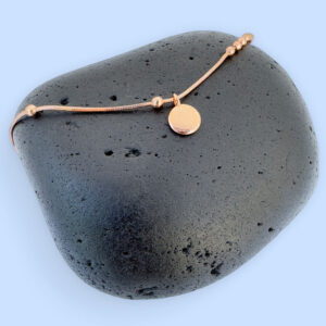Rose gold anklet with a round pendant on a black rock.
