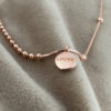 Rose gold anklet, one side with balls close together and another side with just a few far apart. There is a rose gold round pendant with the words lucky written on it in capital letters.