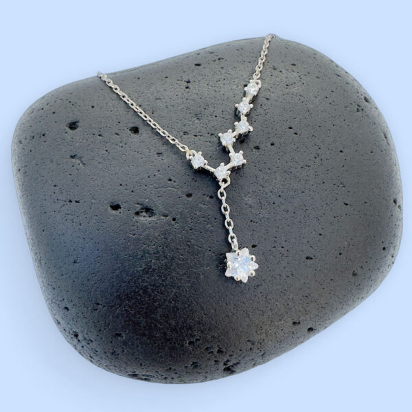 Celestial anklet with seven white gemstones and a large gemstone hanging down, on a black rock.