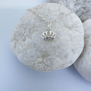 Regal silver anklet with a white gemstone charm and a crown with a white gemstone, on a white rock.