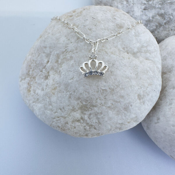 Regal silver anklet with a white gemstone charm and a crown with a white gemstone, on a white rock.
