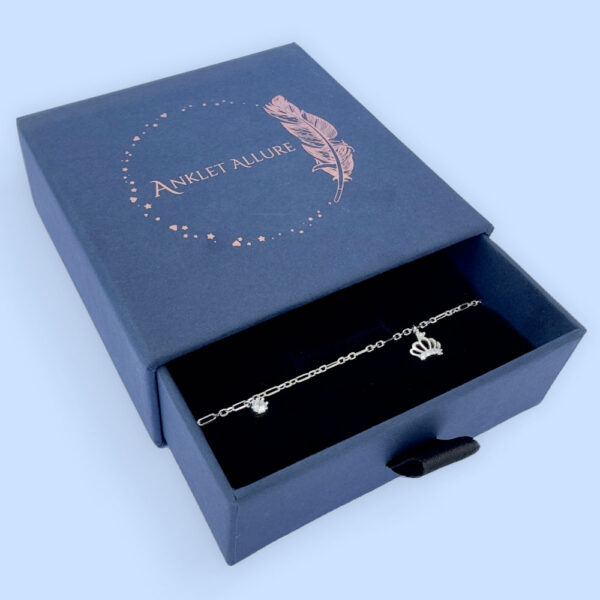 Regal silver anklet with a white gemstone charm and a crown with a white gemstone, in a blue Anklet Allure jewellery box.