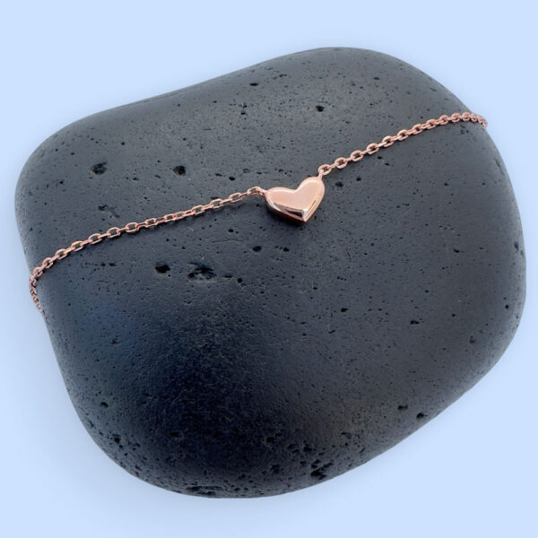 Stunning rose gold anklet with a cute solid rose gold heart charm, on a black rock.