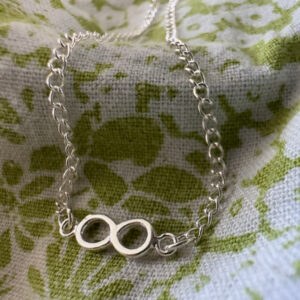Beautiful Infinity anklet presented on a green and white flowered fabric.