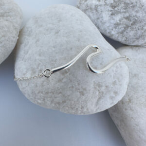 Sterling silver anklet with a surf wave design presented on white rocks.