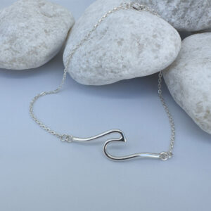 Sterling silver anklet with a surf wave design presented on white rocks.