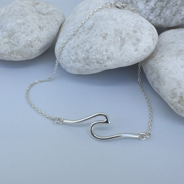 Sterling silver anklet with a surf wave design presented on white rocks.