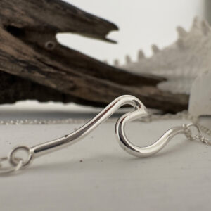 A shiny 925 sterling silver pendant of a rolling wave on an ankle chain displayed in the foreground of the image.