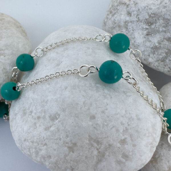 Silver anklet with four turquoise balls evenly spaced around the ankle bracelet, on a white rock.