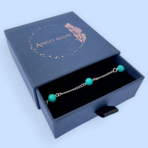 Silver anklet with four turquoise balls evenly spaced around the ankle bracelet, presented in a dark blue Anklet Allure jewellery box.