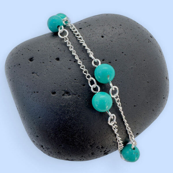 Silver anklet with four turquoise balls evenly spaced around the ankle bracelet, presented on a black rock.