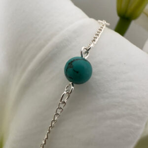 Beautiful turquoise round ball on a shiny silver anklet chain displayed on a petal of a white lily.