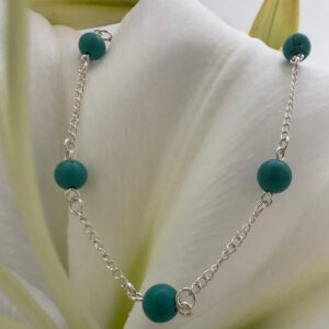 A shiny silver anklet with turquiose balls around the chain, in a beach chic style