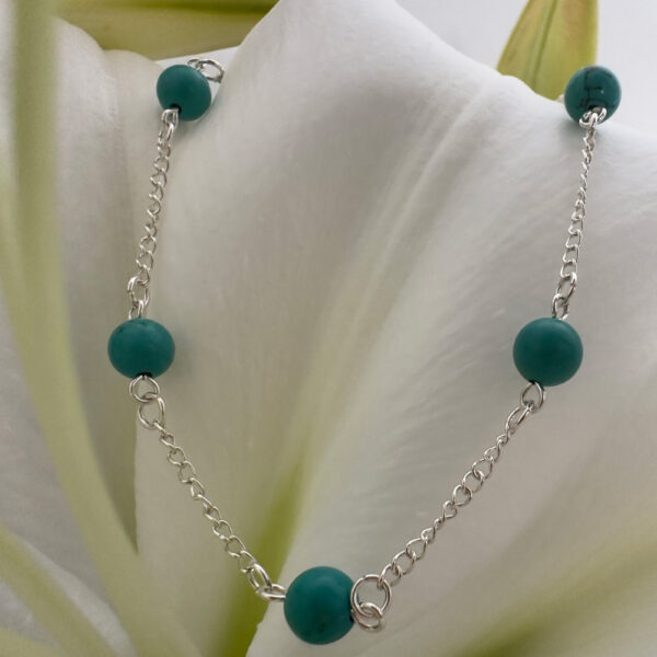 A shiny silver anklet with turquiose balls around the chain, in a beach chic style