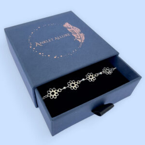 Feminine silver anklets made up of flowers with eight petals linked together with a silver ball in between each flower, presented in a blue Anklet Allure jewellery box.