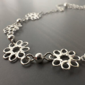 Close up of four pretty sterling silver flowers with eight petals linked together on an ankle bracelet.