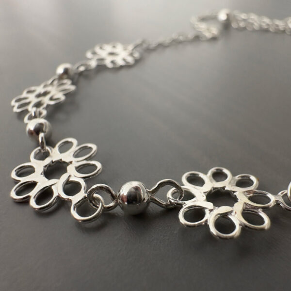 Close up of four pretty sterling silver flowers with eight petals linked together on an ankle bracelet.