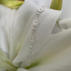 Sterling silver anklet featuring four identical flowers with eight petals each, linked together and draped on a white lily petal for display purposes.