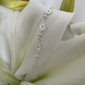 Sterling silver anklet featuring four identical flowers with eight petals each, linked together and draped on a white lily petal for display purposes.