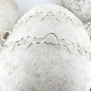 Identical interlinking dainty silver hearts ankle bracelet on a white rock.