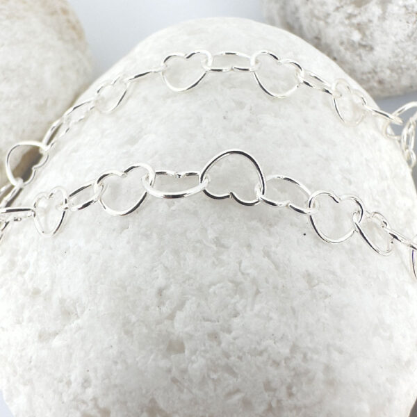 Identical interlinking dainty silver hearts ankle bracelet on a white rock.